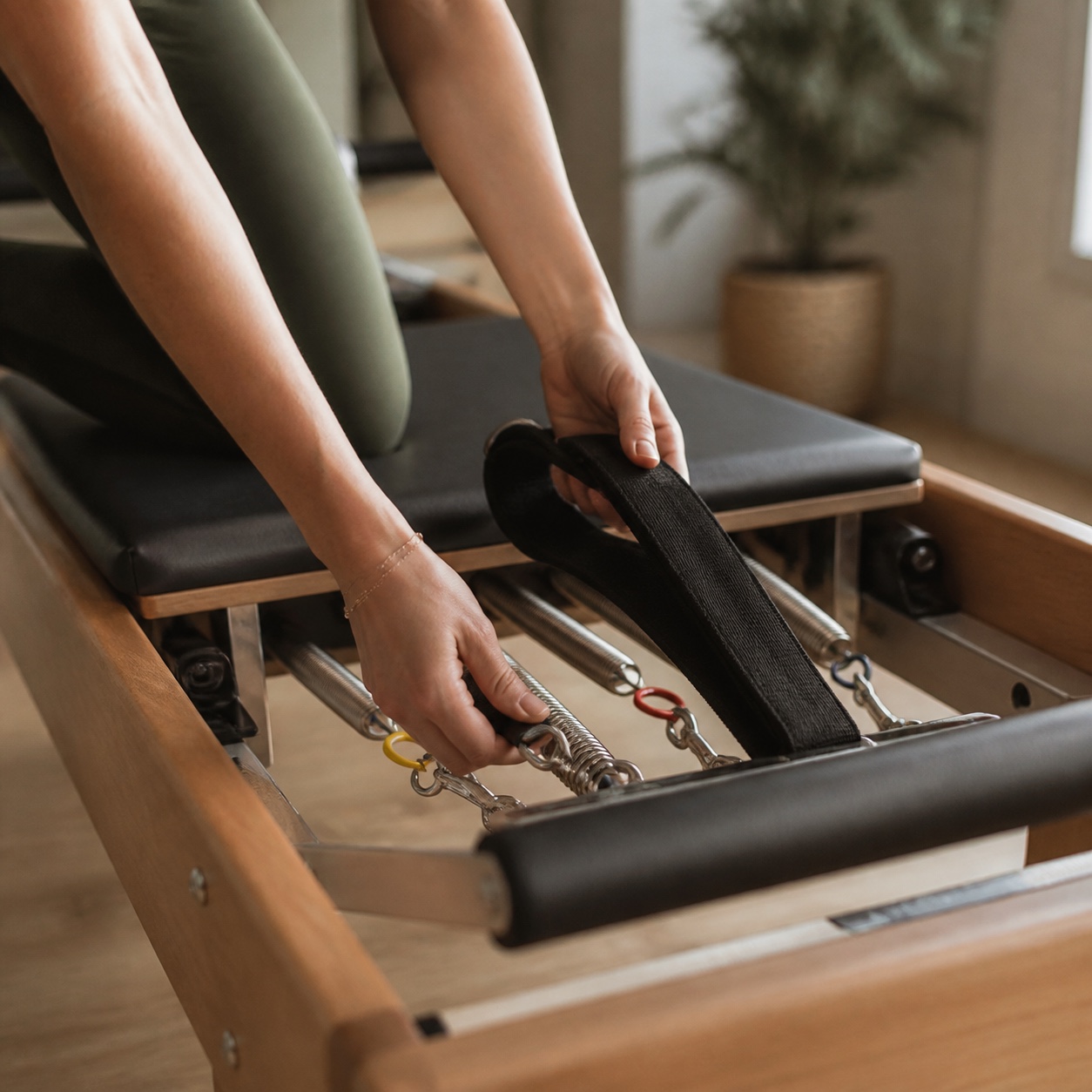 Close-up detail of hands adjusting reformer straps and springs